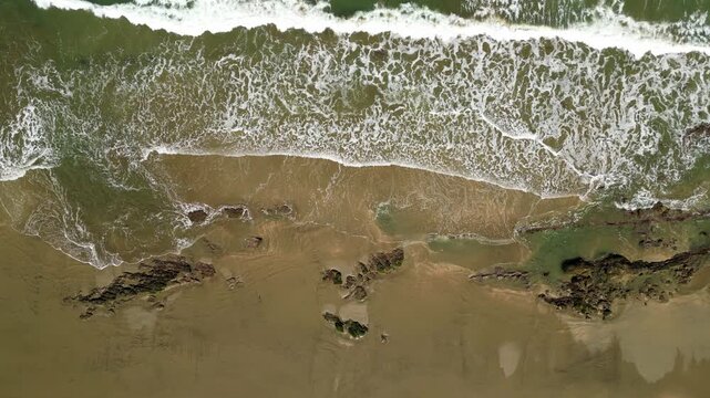 Top down aerial shot of peaceful waves rolling onto a sandy beach in Mancora, Peru