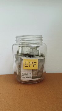 Close up of hand putting india rupee currency note inside transparent glass jar isolated on table with EPF word or text label. Investing money in EPF (Employee Provident Fund) retirement scheme.