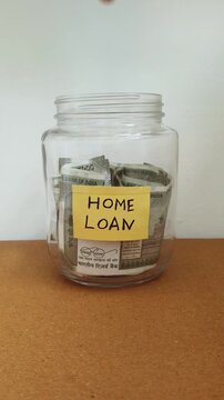 Close up of hand putting india rupee currency note inside transparent glass jar container isolated on table with home loan word or text label. Saving money for repaying house loan emi concept.