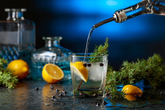 Gin is poured from a bottle into a glass with ice and lemon slice.