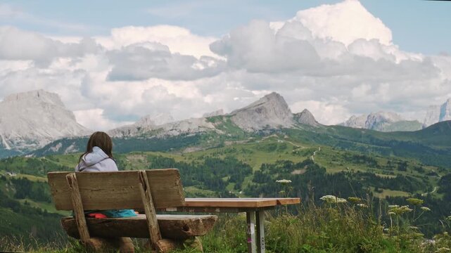 A female hiker finds solitude in the Italian Dolomites, sitting on a wooden bench to admire the scenic mountain landscape. Serene trekking, wellness, and adventure in South Tyrol.Hiking in Italy