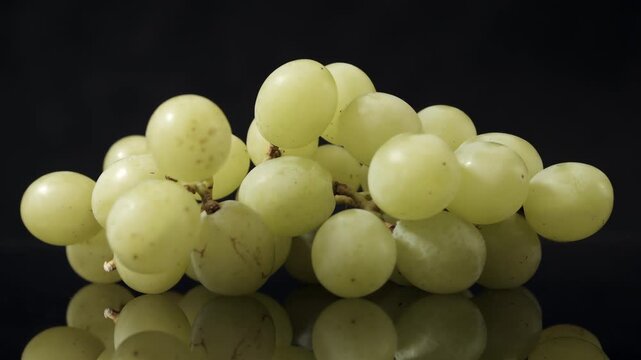 Fresh green grapes clustered on stems rotate slowly against dark background, showing natural surface texture and subtle imperfections in close detail