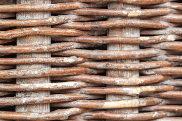 Macro shot of a traditional wicker fence made of intertwined brown wooden branches. Rustic natural texture and rural craft pattern.