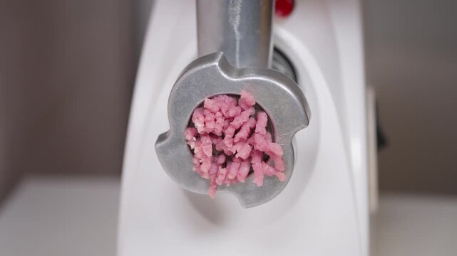 Home chef operates meat grinder smoothly. Electric device producing textured raw beef for cooking. Closeup of meat extrusion with textured strands on clean kitchen surface