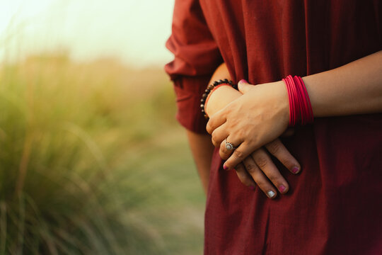 A woman in a red dress standing in a field with her hands clasped behind her back