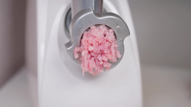 Grinding raw beef and pork for cooking. Home cook uses electric grinder to prepare minced meat. Closeup of manual meat mincing for burgers and sausages on kitchen counter