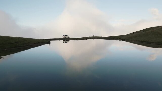 Scenic mirror reflection of a 4x4 vehicle at Koruldi Lakes, Georgia. High altitude alpine landscape in Svaneti, Caucasus mountains. Majestic nature, travel adventure, and calm water.