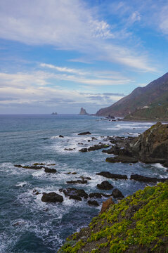 View of the dramatic rocky coast of Anaga near Taganana and Benijos, Tenerife, with ocean waves and unique rock formations under a partly cloudy sky