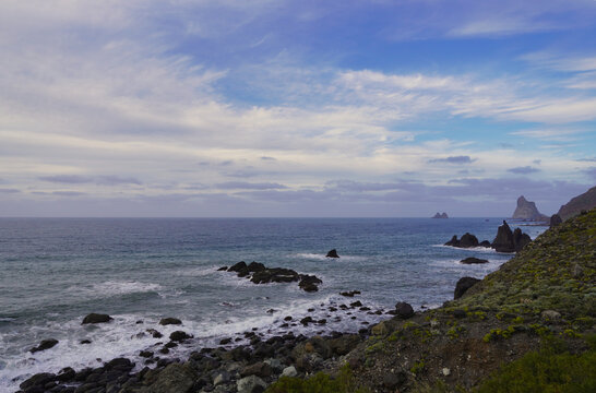 View of the dramatic rocky coast of Anaga near Taganana and Benijos, Tenerife, with ocean waves and unique rock formations under a partly cloudy sky