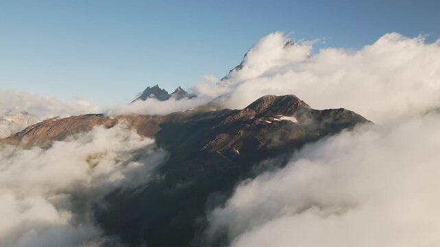 Aerial view of Mount Ushba peak partially covered in morning clouds. A dramatic mountain landscape in Svaneti, Georgia, featuring rugged peaks and atmospheric mist in the Caucasus.
