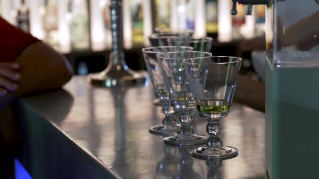 Absinthe glasses lined up on bar counter with green liquor in modern setting