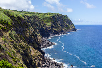 Fototapeta premium Cliffs near Nordeste. Miradouro do Pelado overlooks rocky coastal cliffs and the Atlantic. Green slopes meet deep blue ocean. Sao Miguel. Azores. Portugal.