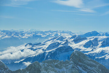 Naklejka premium Snow covered mountain range under clear blue sky, showcasing majestic peaks and ridges. serene landscape is enhanced by scattered clouds, creating breathtaking view of nature beauty