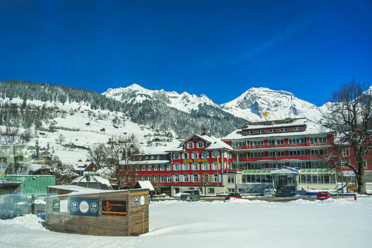 28-03-2026 Santis Switzerland, Snow covered alpine village with red hotel, surrounded by majestic mountains under clear blue sky. serene winter landscape evokes sense of tranquility and adventure