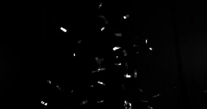 Silver confetti flying in super slow motion against a black background. Shiny metallic particles drifting and falling in the air, creating elegant festive atmosphere with dramatic lighting. Speed ramp