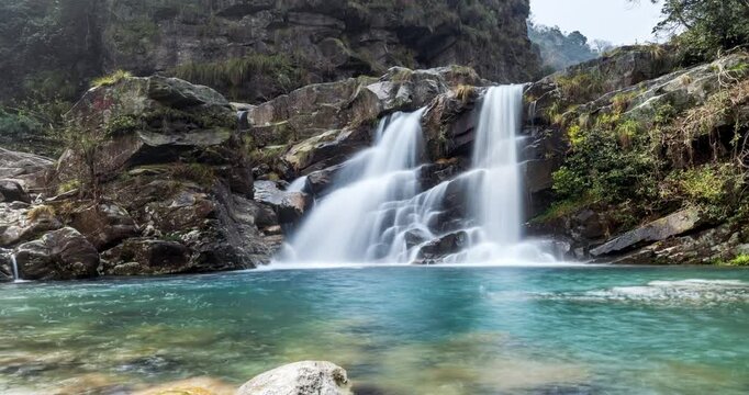Time-lapse of the silky twin waterfalls cascade through a lush valley, with emerald pools and glacial rocks under soft spring light, Lushan mountain, Jiangxi Province, China.