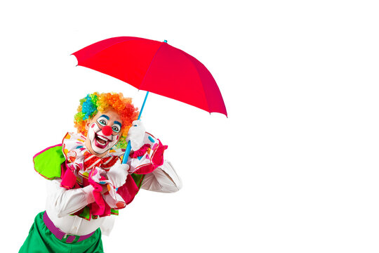 Funny clown holding orange umbrella. Entertainer Joker in colorful suit and wig. Buffoon with clown whiteface makeup. Professional actor at event, kid's party, circus