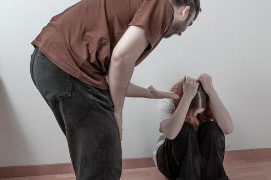 Aggressive man confronting a frightened woman in a room as she hides her face, showing abuse, coercive control, family conflict, fear and trauma at home.