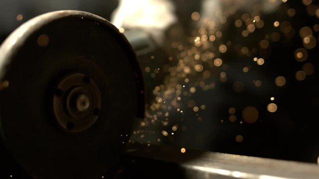 A worker uses a grinding tool on metal. Sparks fly from the process as the worker focuses on the task. The activity takes place in a workshop setting with dim lighting.