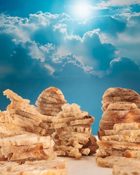 In a dreamlike landscape, towering formations of bread rise like mountains beneath a vibrant blue sky sprinkled with fluffy clouds. Light dances playfully across this surreal scene