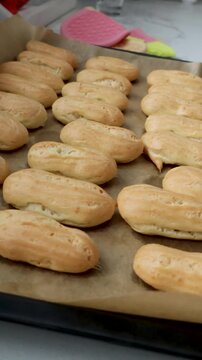 Fresh baked choux pastries on sheet in sunny kitchen. Golden eclairs cooling after oven for cream filling. Homemade dessert preparation sequence for custard treats. video footage video footage