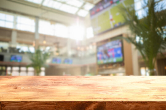 wooden table on foreground and blurred background depicts the lively interior of a sports bar