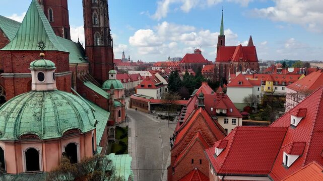 Cinematic drone flight over historic Ostrow Tumski in Wroclaw, featuring close-up views of St. John the Baptist Cathedral, green domes, red rooftops, and unique architecture of the city's oldest distr