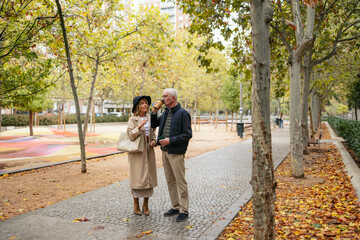 Fototapeta premium Senior couple enjoying coffee and conversation while walking together in a city park