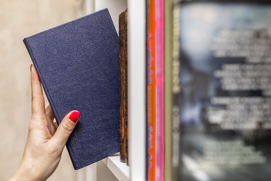 a woman's hand takes a blue book from the shelf. female picking blue book from bookshelf, close-up. Hand picking up book on bookshelf in library. 