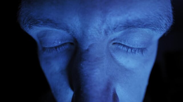 Extreme close-up of a male face distorted by a wide-angle lens features eyes darting around suspiciously. Dramatic blue lighting creates a paranoid and eerie atmosphere.
