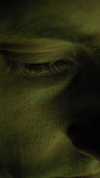 A macro shot details the closed eye and eyelashes of a person resting in dark, moody green illumination. Concept of REM sleep, dreaming, medical examination, or mysterious sci-fi atmosphere.