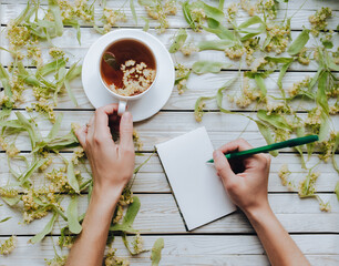 The girl doctor writes a prescription to the patient. Influenza, acute and respiratory diseases. Tea in a cup of dried flowers of lime on a wooden background. Full recovery, copy space.