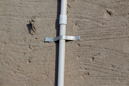 Close up of PVC water pipe fixed on wall with metal clamp support for household plumbing installation system