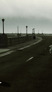 An astronaut stands alone on an empty road next to the ocean. The sky is cloudy and grey. There are lamp posts along the road, adding to the unusual scene.