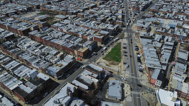 Open lot residential grid near S 8th St and Wolf St reveals dense rowhome blocks broken by a central green parcel. Light roofs, brick facades, and warm directional light in Philadelphia, PA