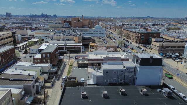 Port edge residential sweep near S 12th St and Pattison Ave shows dense housing stretching toward industrial cranes along the Delaware River. Flat roofs, muted tones, soft haze shape Philly, PA