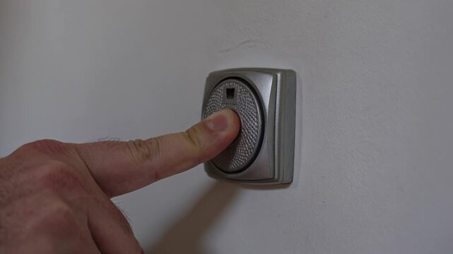 Man pressing a silver modern doorbell button on a wall