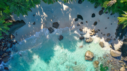 erial drone view of Tusculum Beach in Mahé, Seychelles, showcasing pristine white sand framed by striking granite boulders. Crystal-clear turquoise waters gently meet the shore © Nils