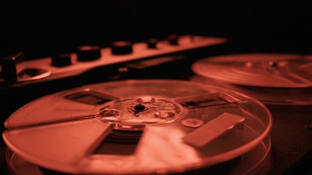 A vintage reel-to-reel tape recorder plays in a dark, mysterious room illuminated by a dramatic red light. This represents concepts of analog recording, surveillance, and nostalgia.
