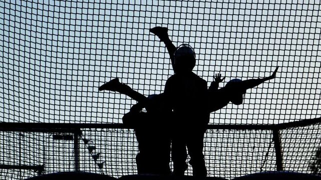 Kids playing on trampoline through safety net, jumping high for joy and freedom