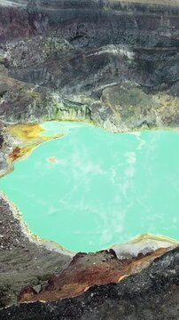 Aerial drone view of a turquoise crater lake inside a volcanic crater in Guatemala, surrounded by rugged volcanic rock formations and geothermal landscape. Vertical