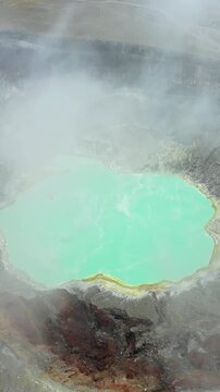 Aerial drone view of a turquoise crater lake inside a volcanic crater in Guatemala, surrounded by rugged volcanic rock formations and geothermal landscape. Vertical