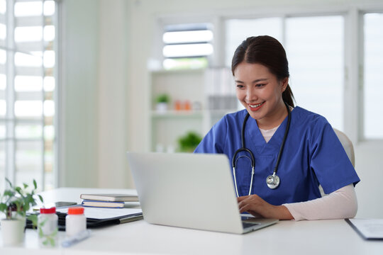 Asian female doctor nurse working laptop computer telemedicine patient care medical office healthcare professional smiling digital health remote work