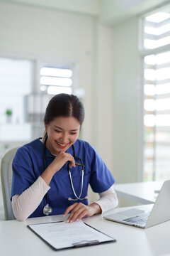 Asian adult healthcare professional reviews patient documents at modern clinic office smiling working medical consultation happy doctor nurse practitioner records management