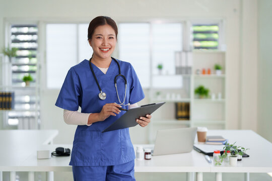 Asian adult healthcare professional nurse doctor holding clipboard pen smiling confident modern medical office clinic hospital standing happy professional