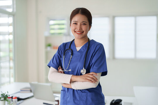 Asian adult nurse smiles confident professional pose arms crossed wearing scrubs stethoscope healthcare facility support patient care
