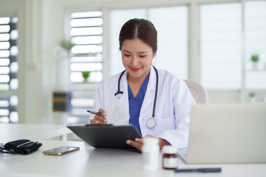 Asian female doctor medical professional reviewing patient records documents clinic office healthcare smiling adult physician professional services