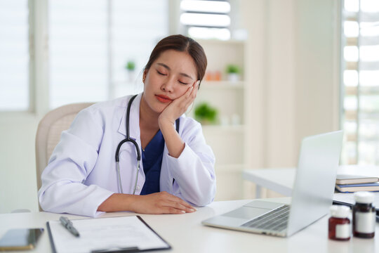 Asian adult female doctor feeling exhausted resting head on hand sleeping desk office after long shift working healthcare professional burnout fatigue stress concept