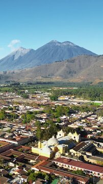 Aerial drone view of Antigua Guatemala city with Volcan de Agua rising dramatically in the background. Vertical