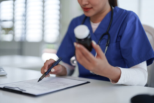 Asian adult doctor nurse healthcare worker examining medicine bottle writing patient report filling prescription documents medical clinic hospital office